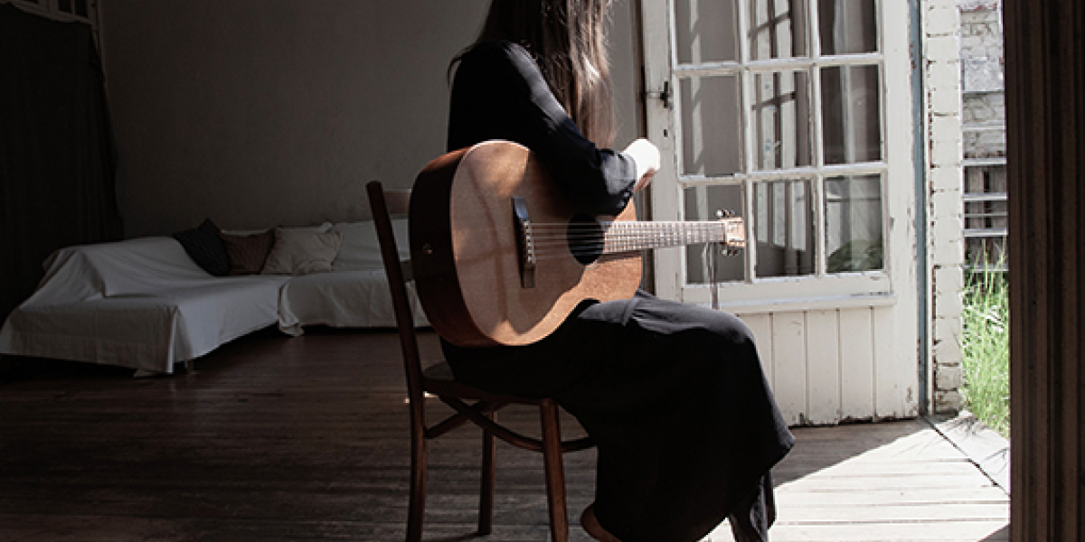 Vrouw met gitaar zit met rug naar kijker toe