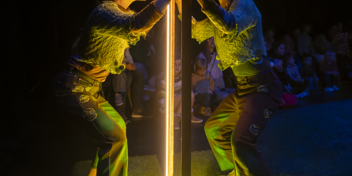 2 acteurs, ieder aan een kant van een raam met 2 spots erop gericht op een groen stukje gras